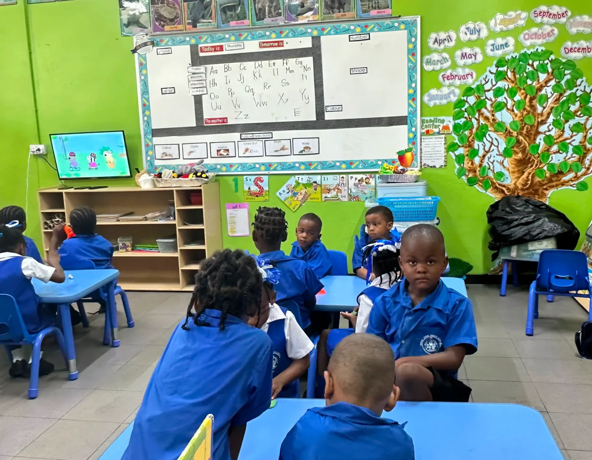 A group of children sitting at tables in front of a board.